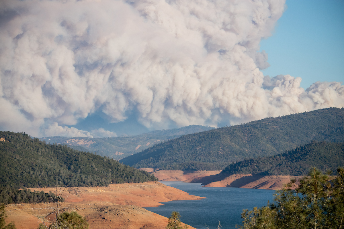 A massive smoke plume from the Butte County, Camp Fire covers the distant sky above the North Fork of Lake Oroville in Northern California.